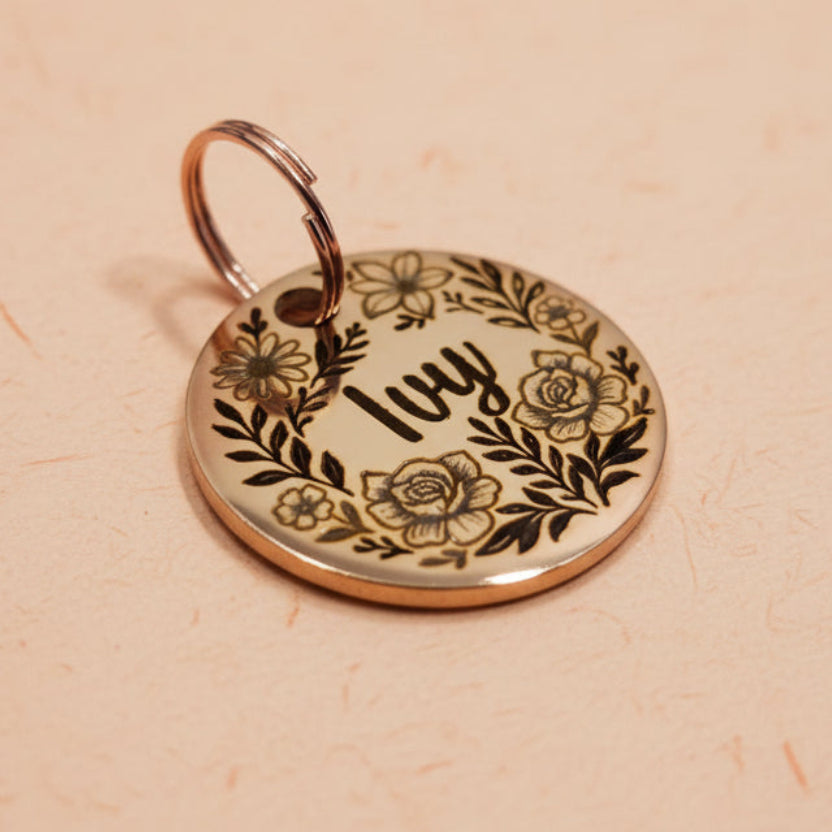 Round rose gold dog tag with floral design and engraved name on a wooden surface