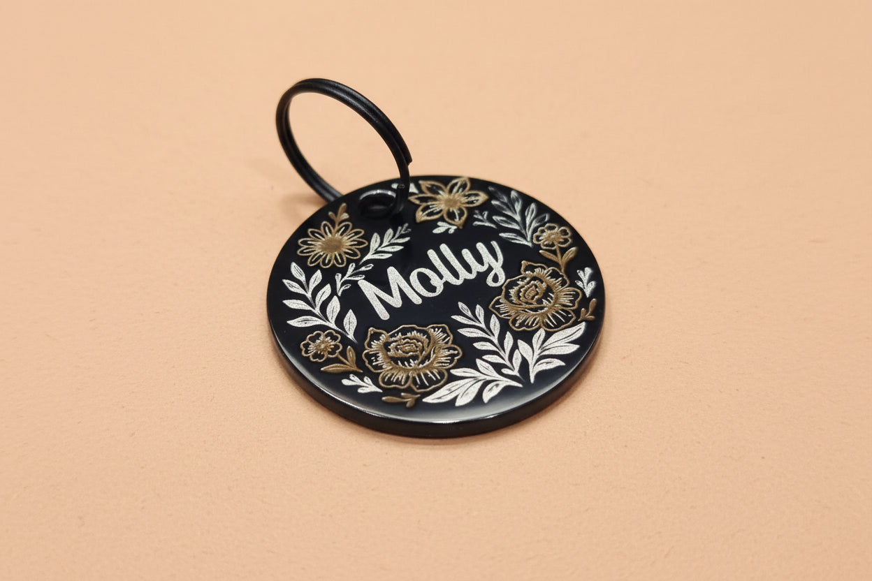 Round black dog tag with floral design and name engraved on it