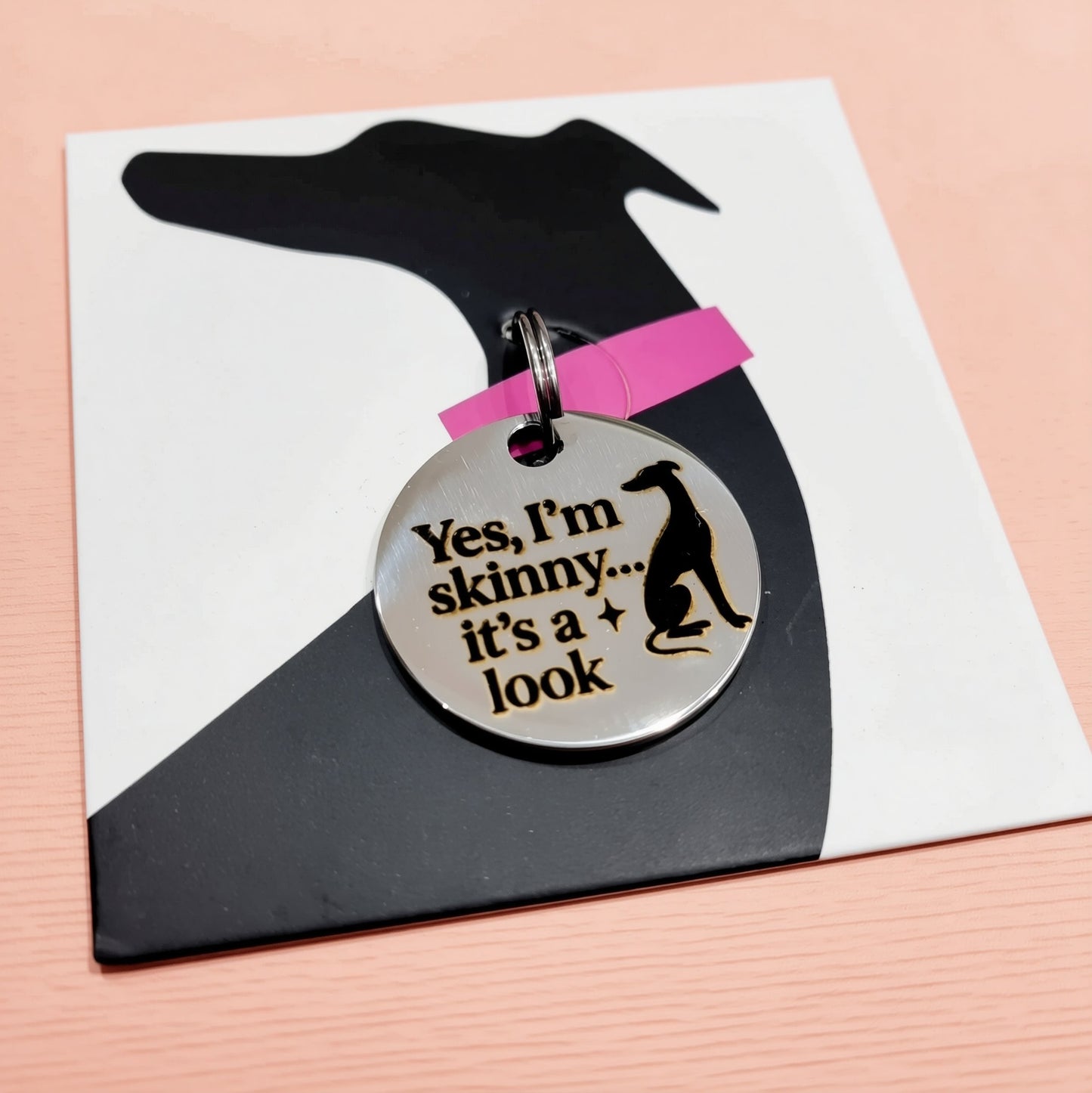 A black and white dog tag with a humorous text that reads "Yes, I'm skinny... it's a look".