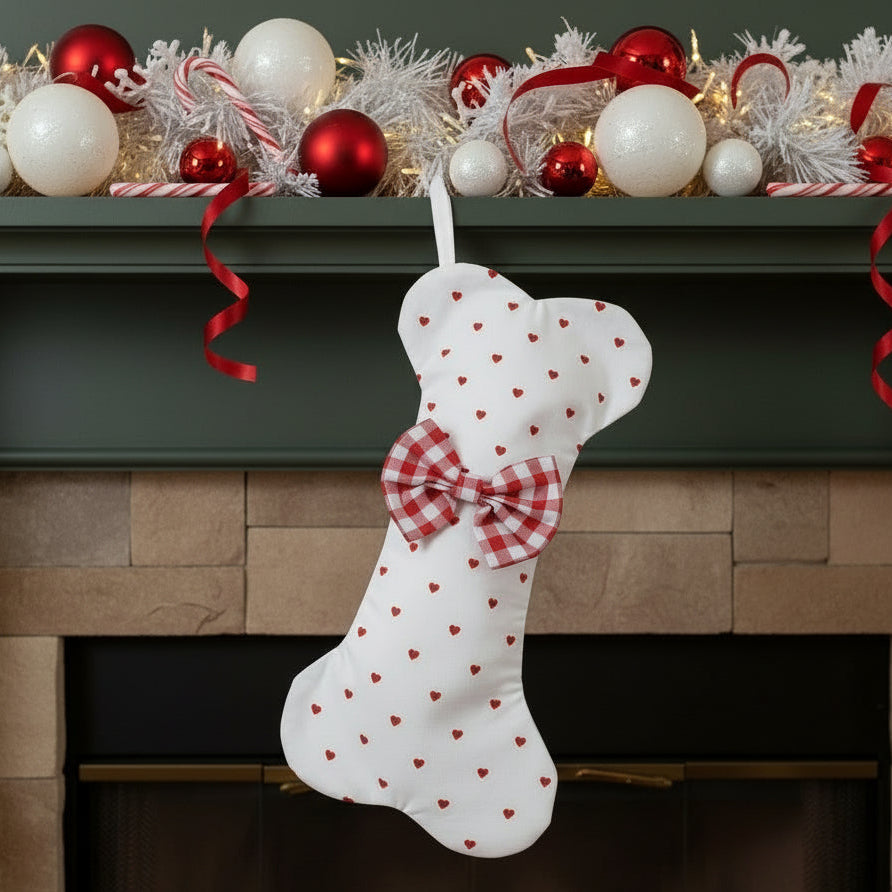 White Dog Christmas stocking with red heart patterns and a bow, hanging on a fireplace mantle decorated with festive ornaments.